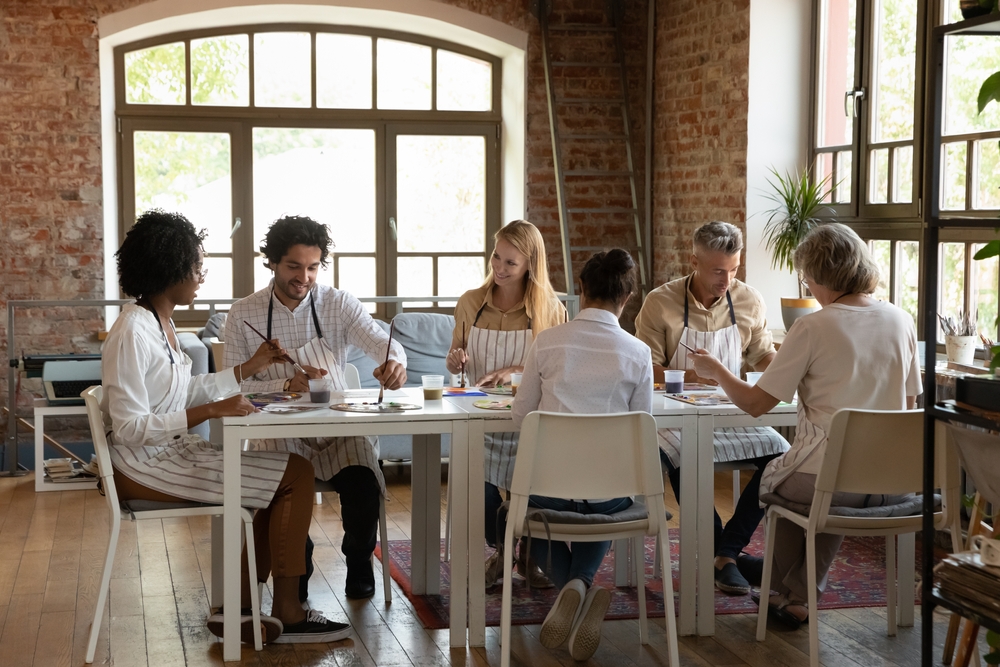 six people painting while seated at a white table