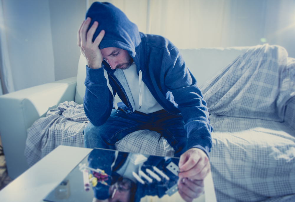 man looking sad with lines of on a table cocaine