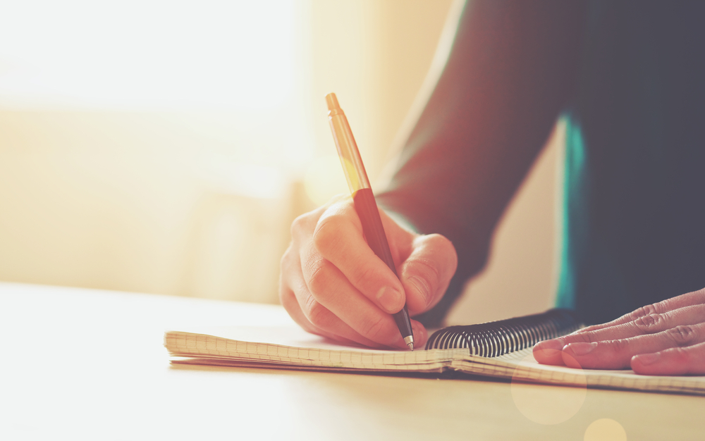 person writing with a pen in a notebook